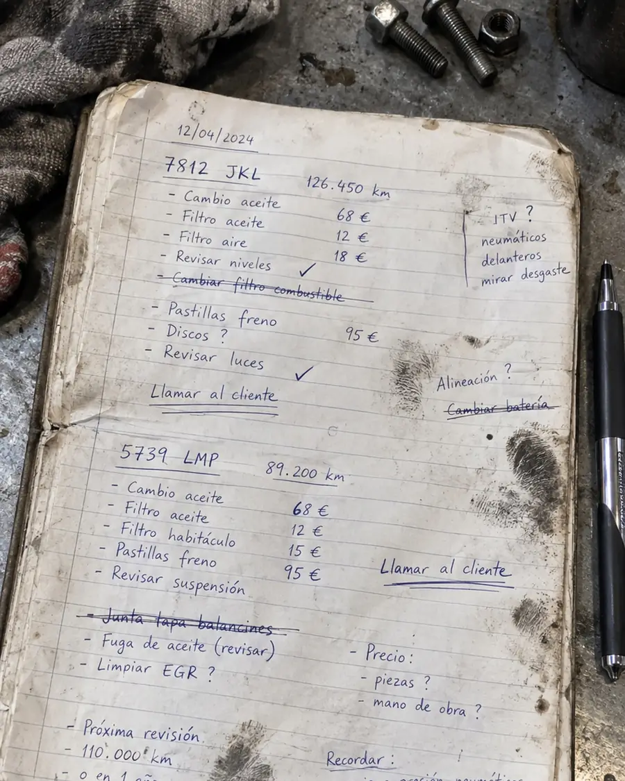 Libreta de taller manchada de grasa con matrículas, piezas e importes a medio apuntar